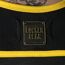Detalle del distintivo Locker Gear sobre tejido negro perforado con ribete amarillo
