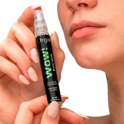 Manos sosteniendo el spray Orgie WOW junto a los labios