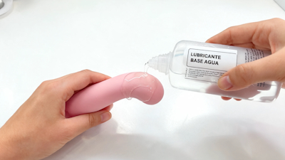 Persona aplicando lubricante base agua transparente en un vibrador de silicona rosa