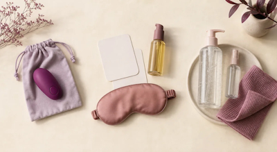 Bala vibradora morada, antifaz rosa, tarjetas, bolsa y dos frascos sobre fondo claro