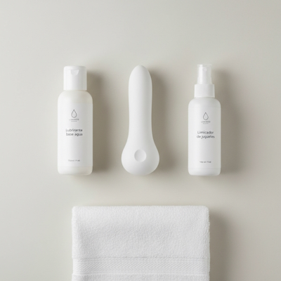 Dildo junto a lubricante base agua y limpiador de juguetes sexuales sobre toalla blanca